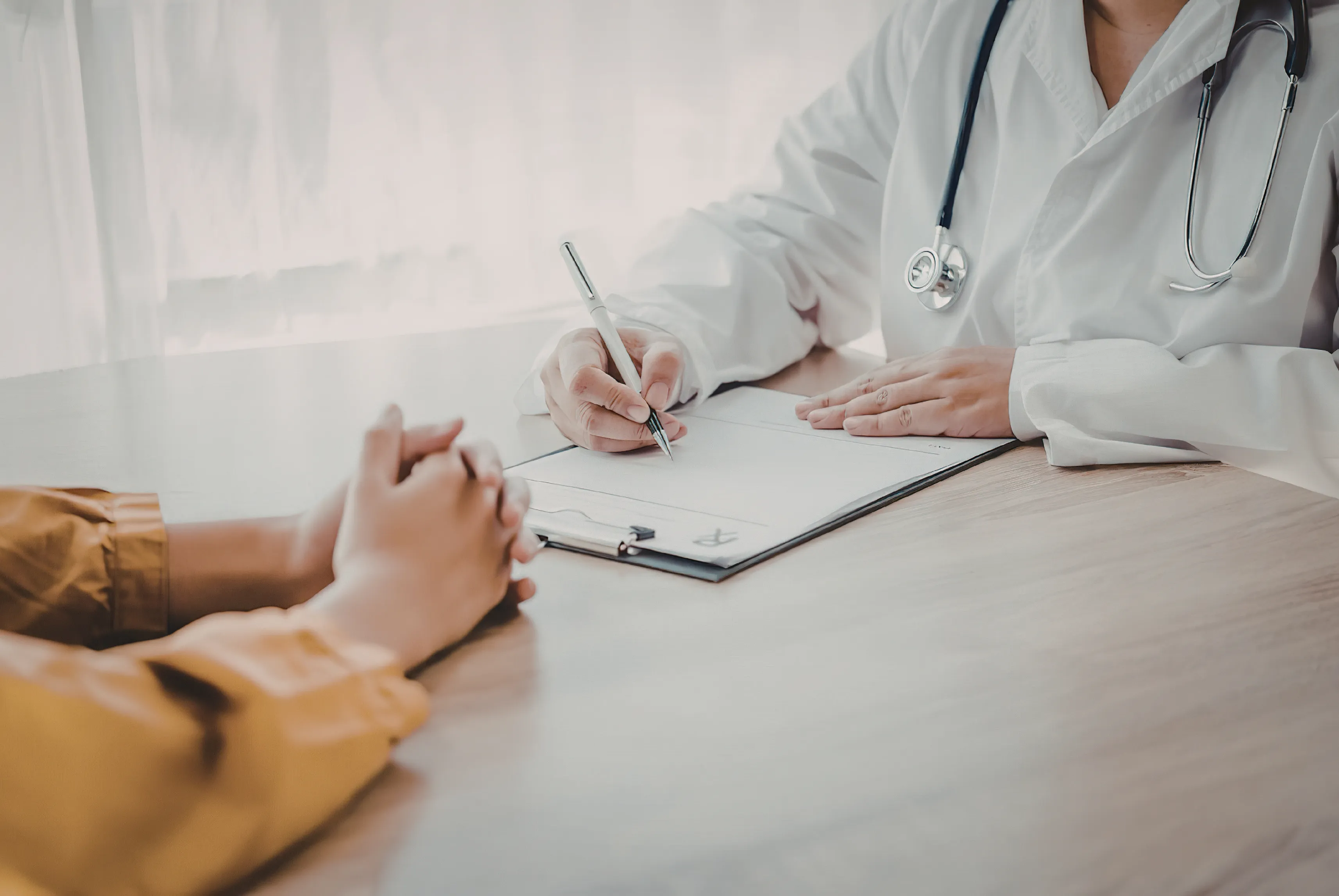 A practitioner and a client talking across a desk, notes being written on a clipboard.